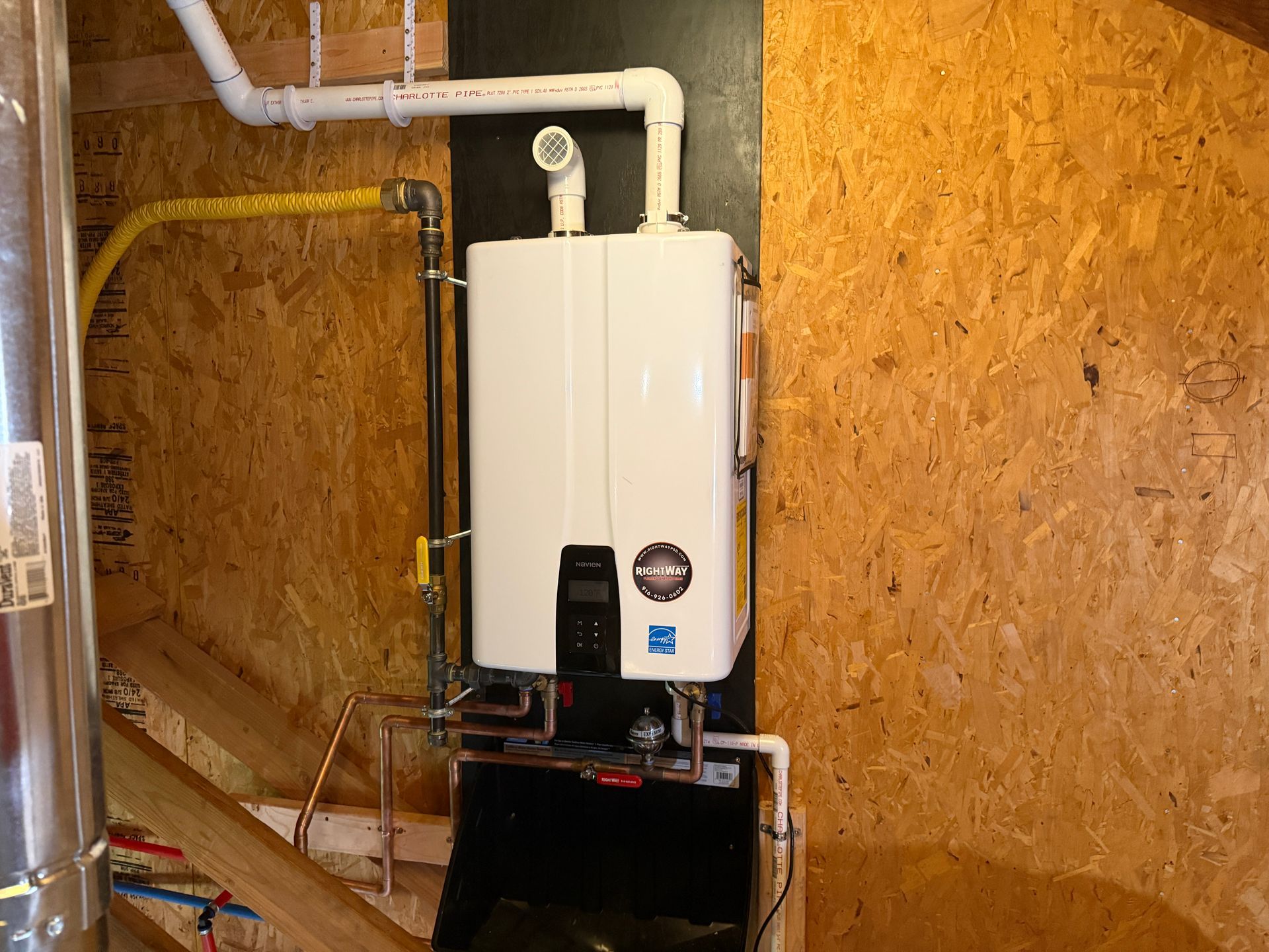 Wall-mounted white water heater with pipes and gauge in a plywood utility room