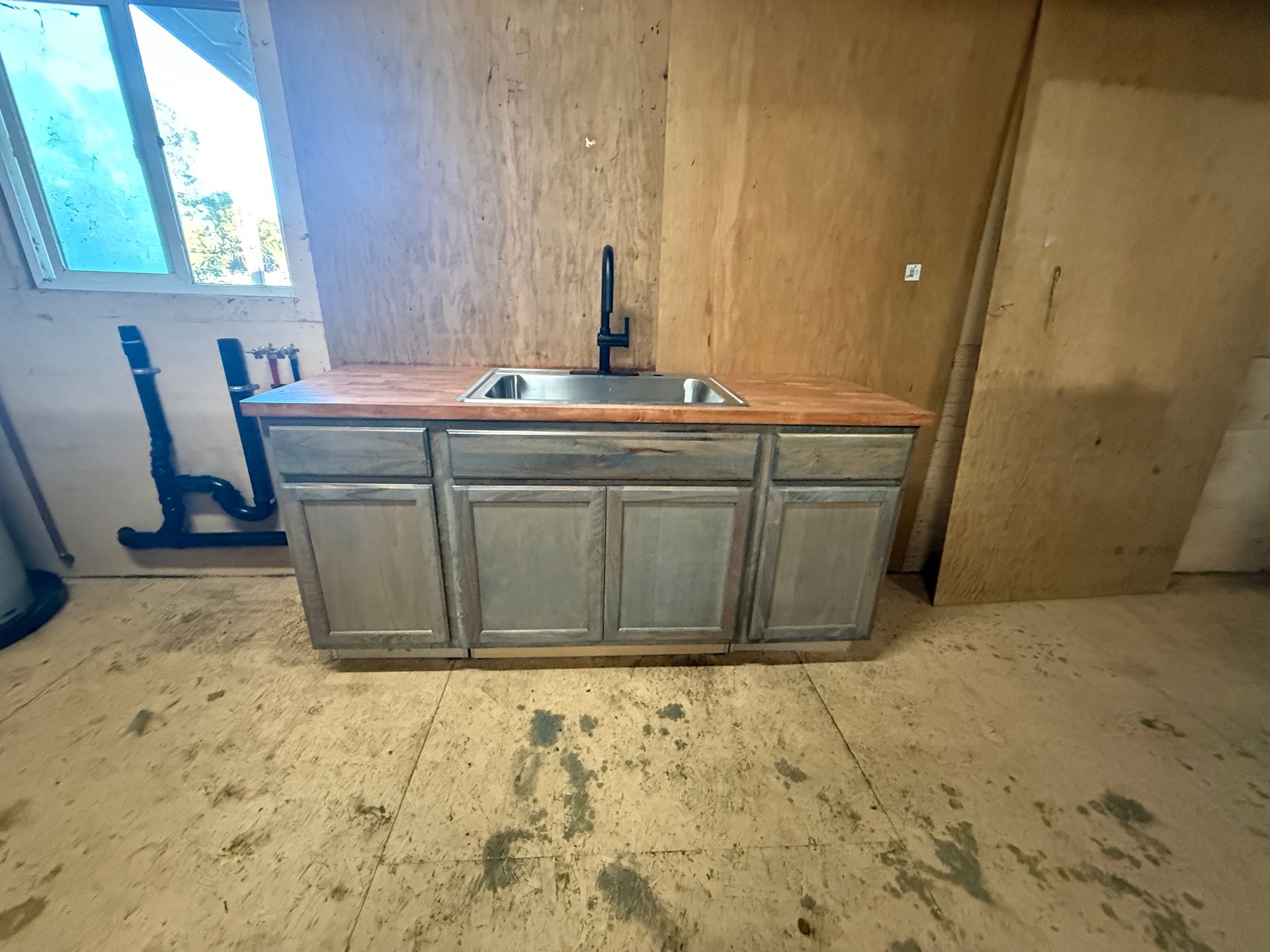 Kitchen sink cabinet in an unfinished room with wood-paneled walls and a dirty concrete floor.