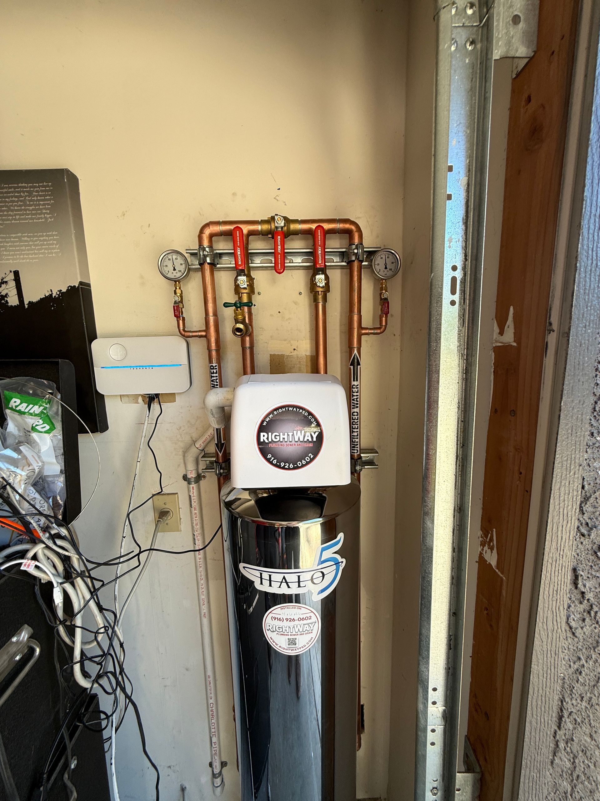 Water softener and plumbing pipes installed against a wall in a utility closet