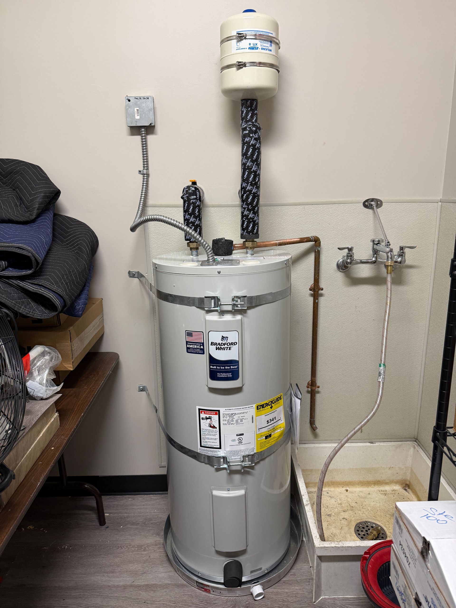 Tall gray water heater in utility room with pipes, expansion tank, and nearby utility sink