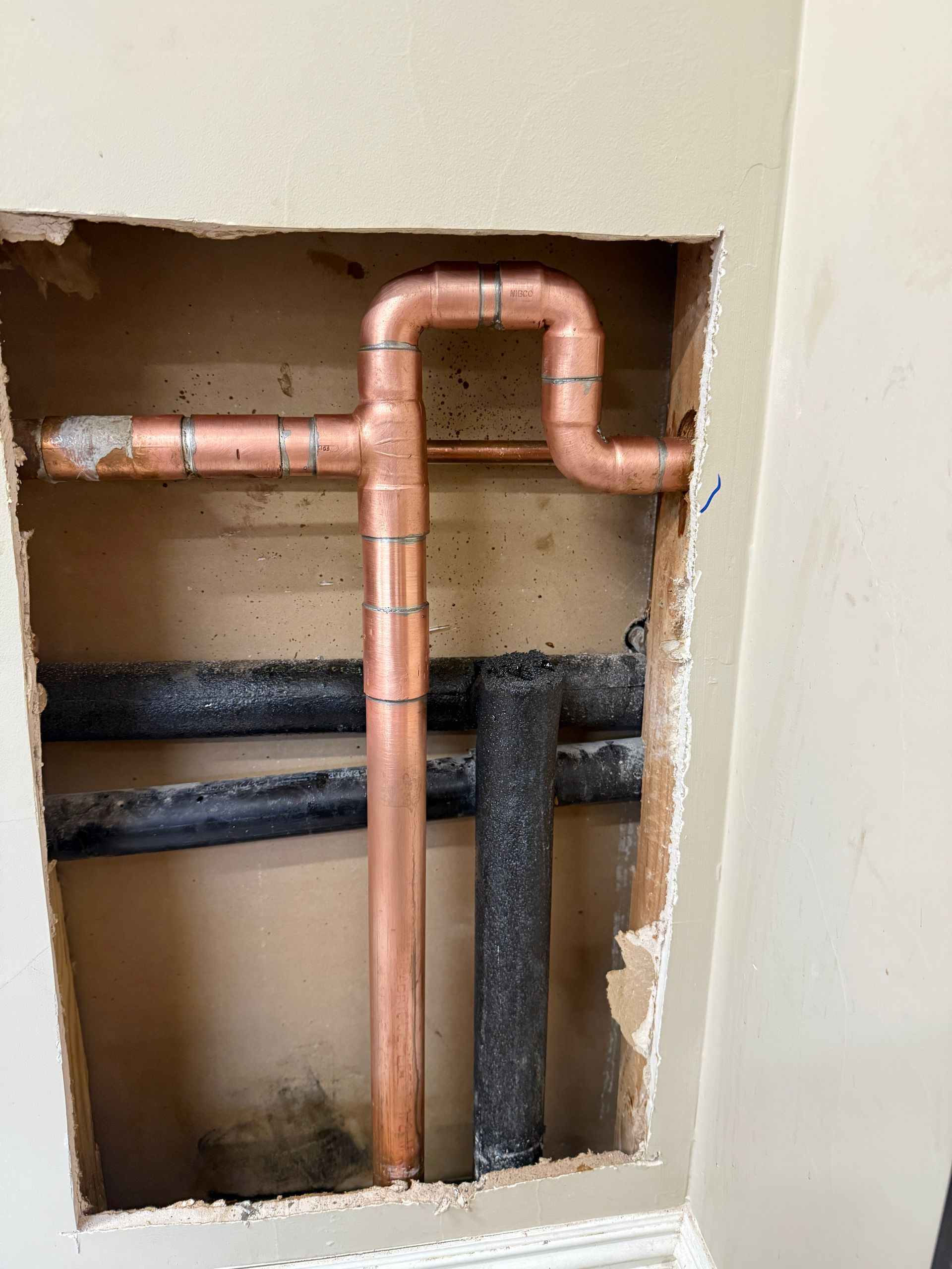 Copper and black plumbing pipes in a rough wall opening during construction.