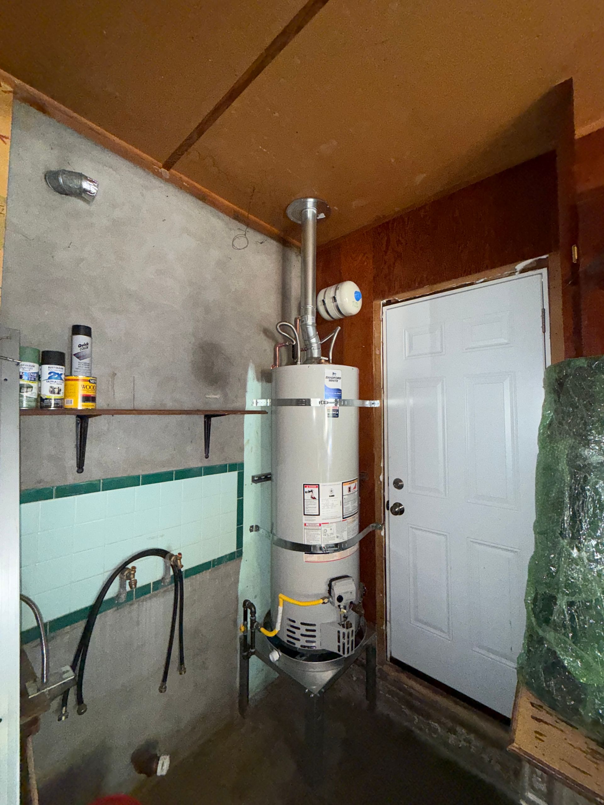 Basement utility room with water heater, pipes, white door, and concrete walls
