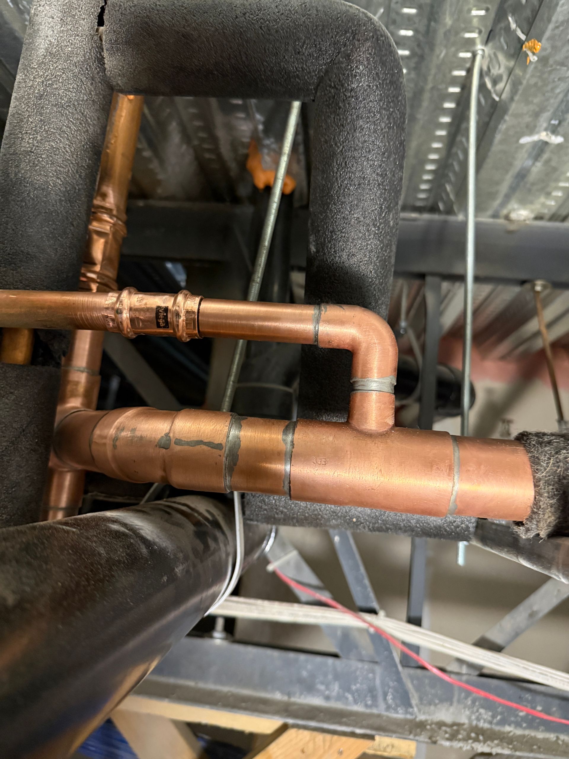 Copper HVAC pipes and black insulated ductwork inside a building ceiling cavity.
