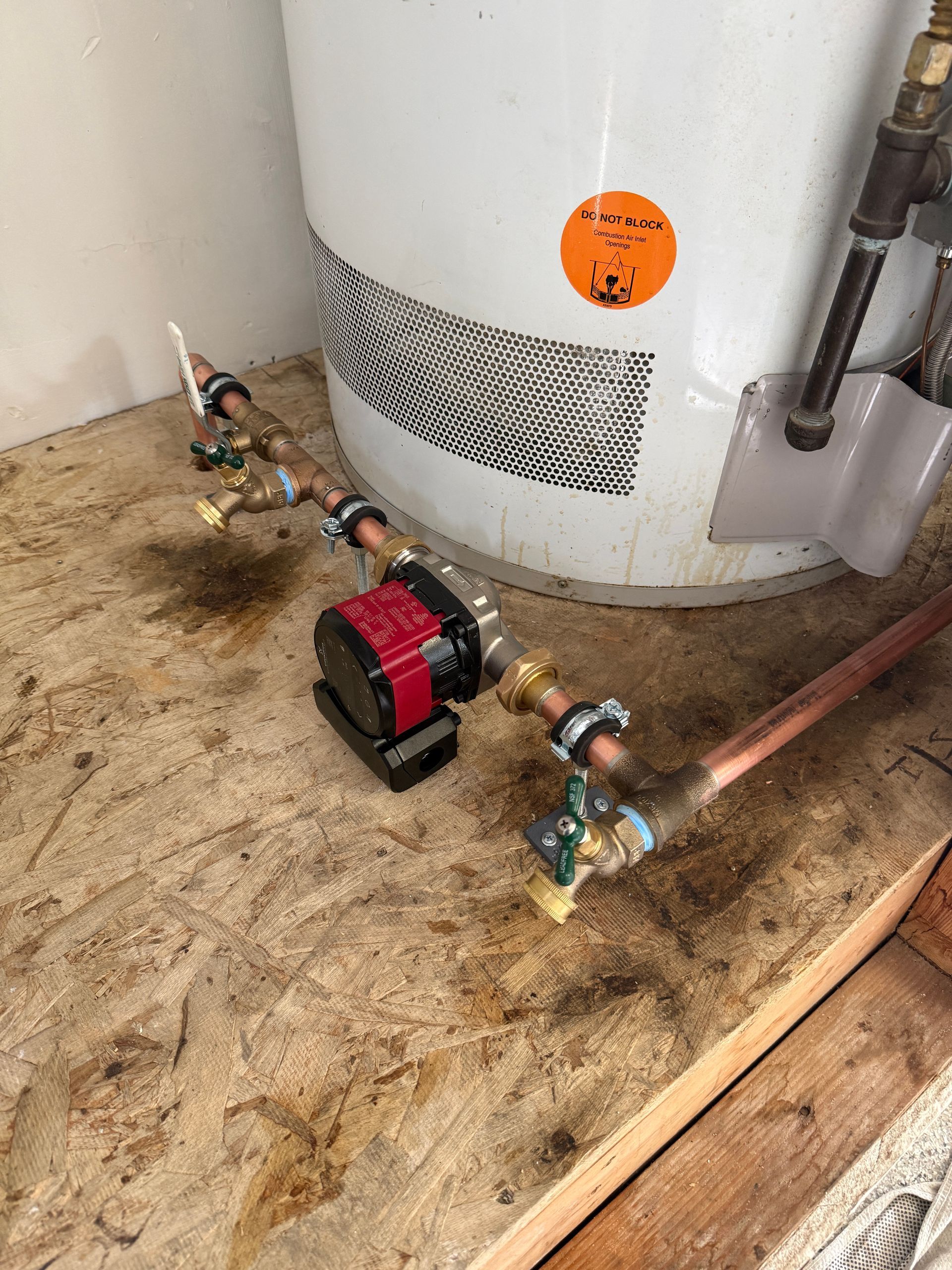 Water heater with small pump and copper piping on a dirty utility-room floor