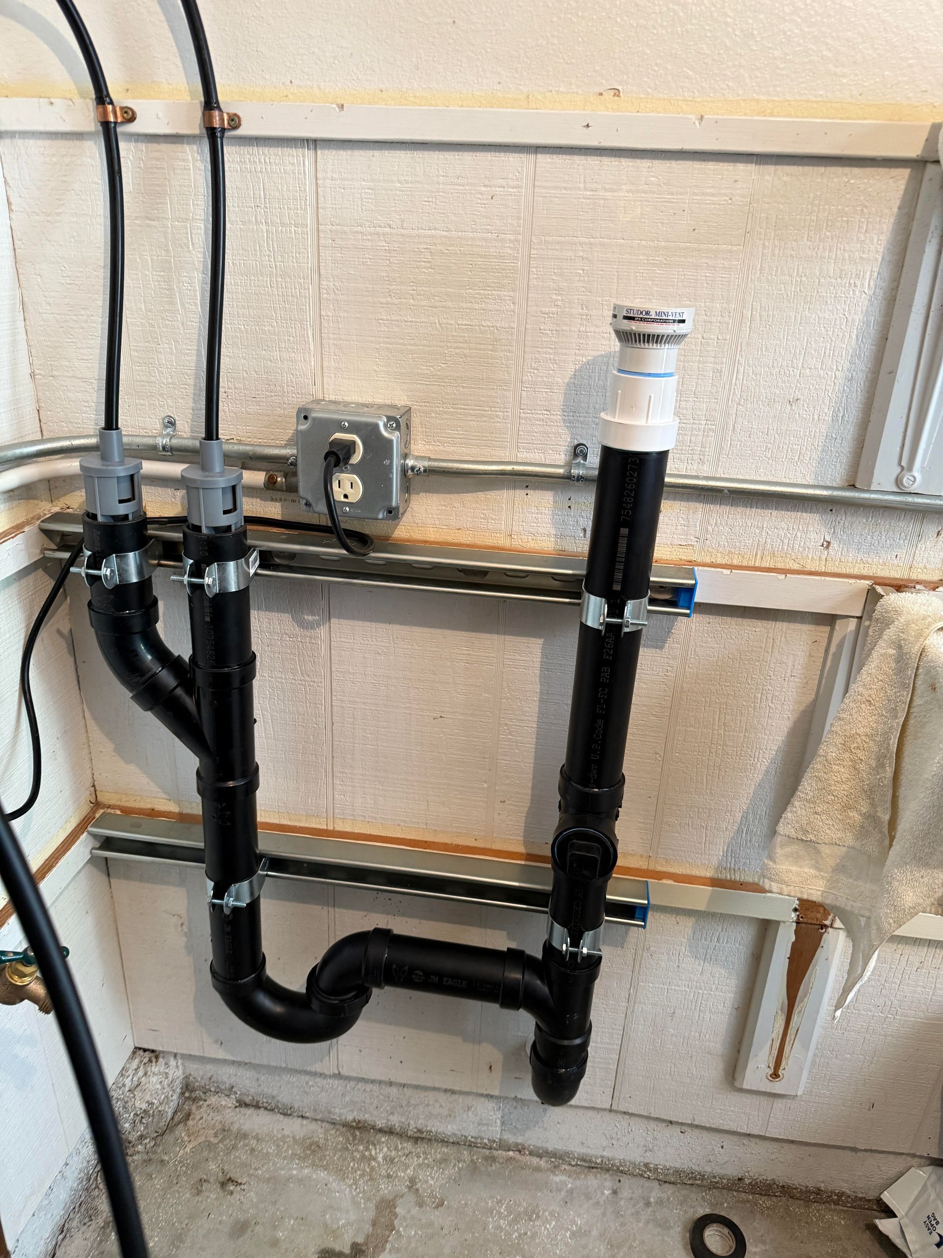 Rightway Plumbing Sewer And Drain -Black plumbing pipes against a gray concrete wall. Electrical outlets and wires.