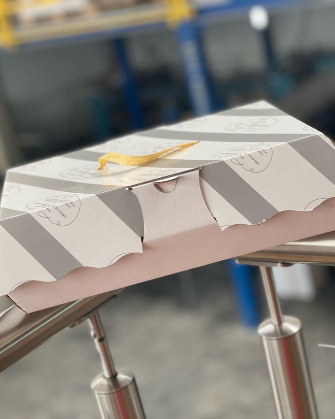 Modellino di carta bianca piegata con una clip gialla su un supporto metallico in un ambiente di officina.