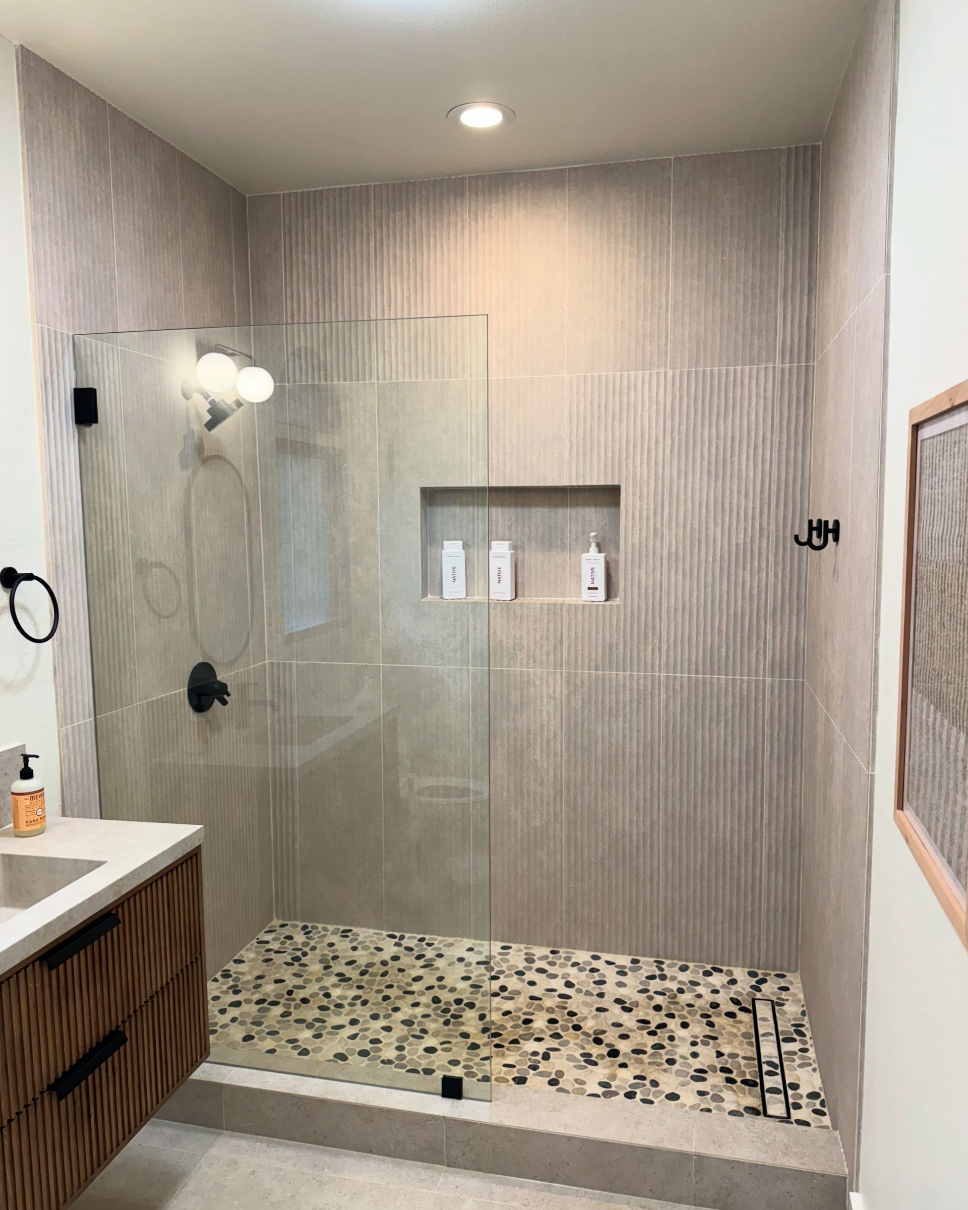 Modern bathroom with a glass door, textured tile walls, and a pebble floor.