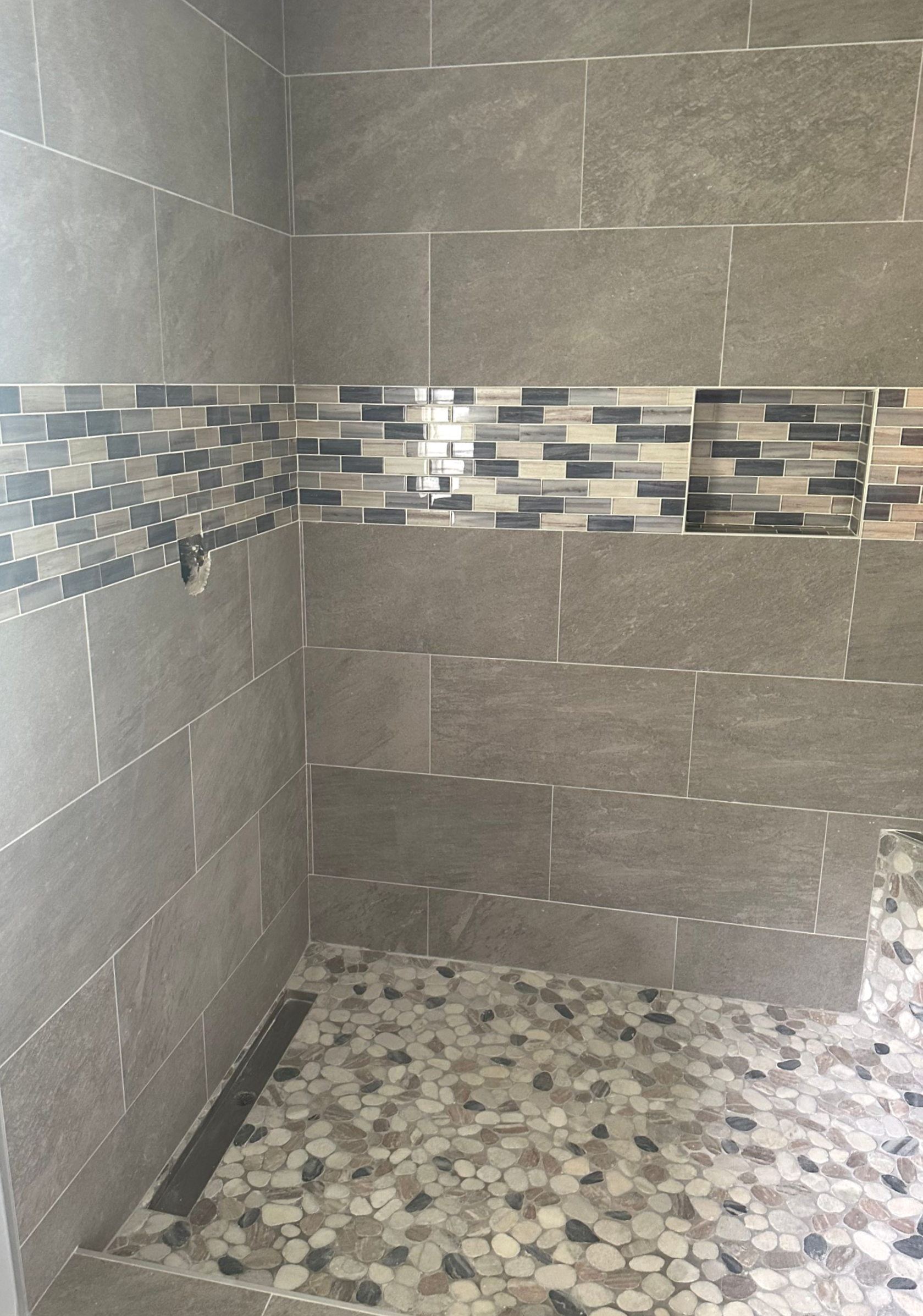 Gray tiled shower with pebble floor and mosaic accent.