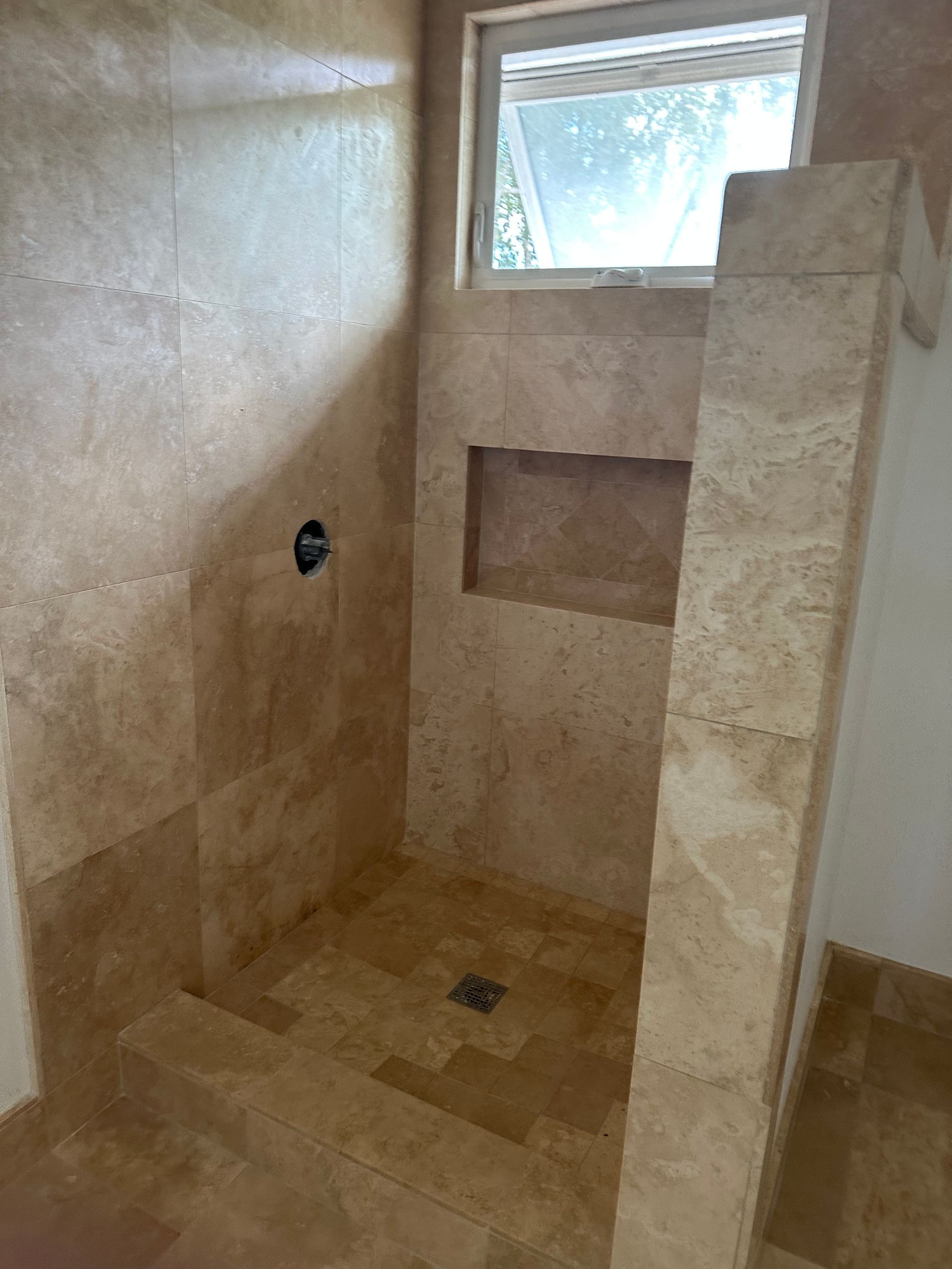 A marble shower with a niche and window. 