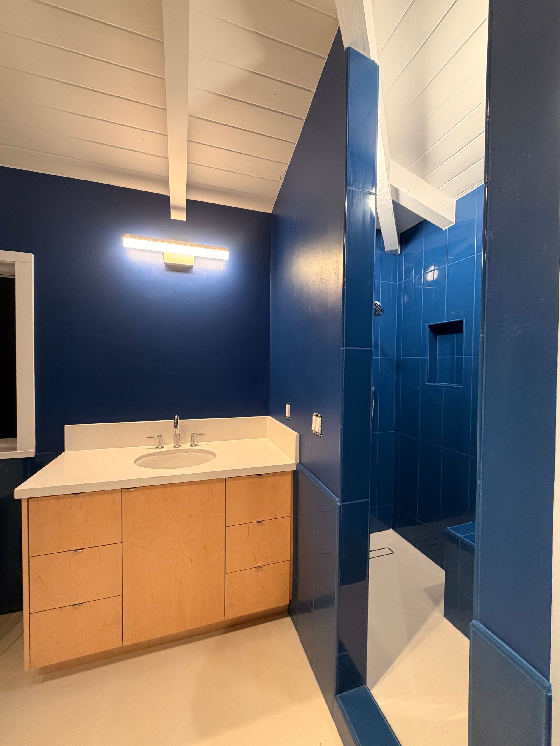 Blue bathroom with wood vanity, white quartz countertop, and shower. 
