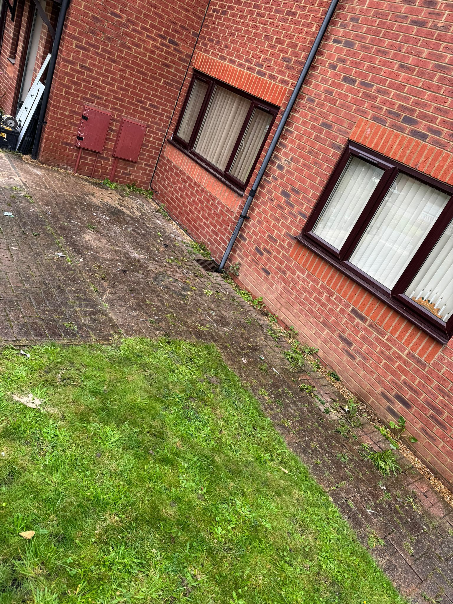 Brick building with two windows, a concrete path, and a patch of grass.
