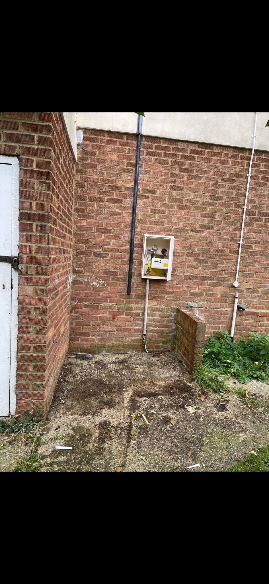 Brick building exterior with a utility box, a small brick structure, and some vegetation.