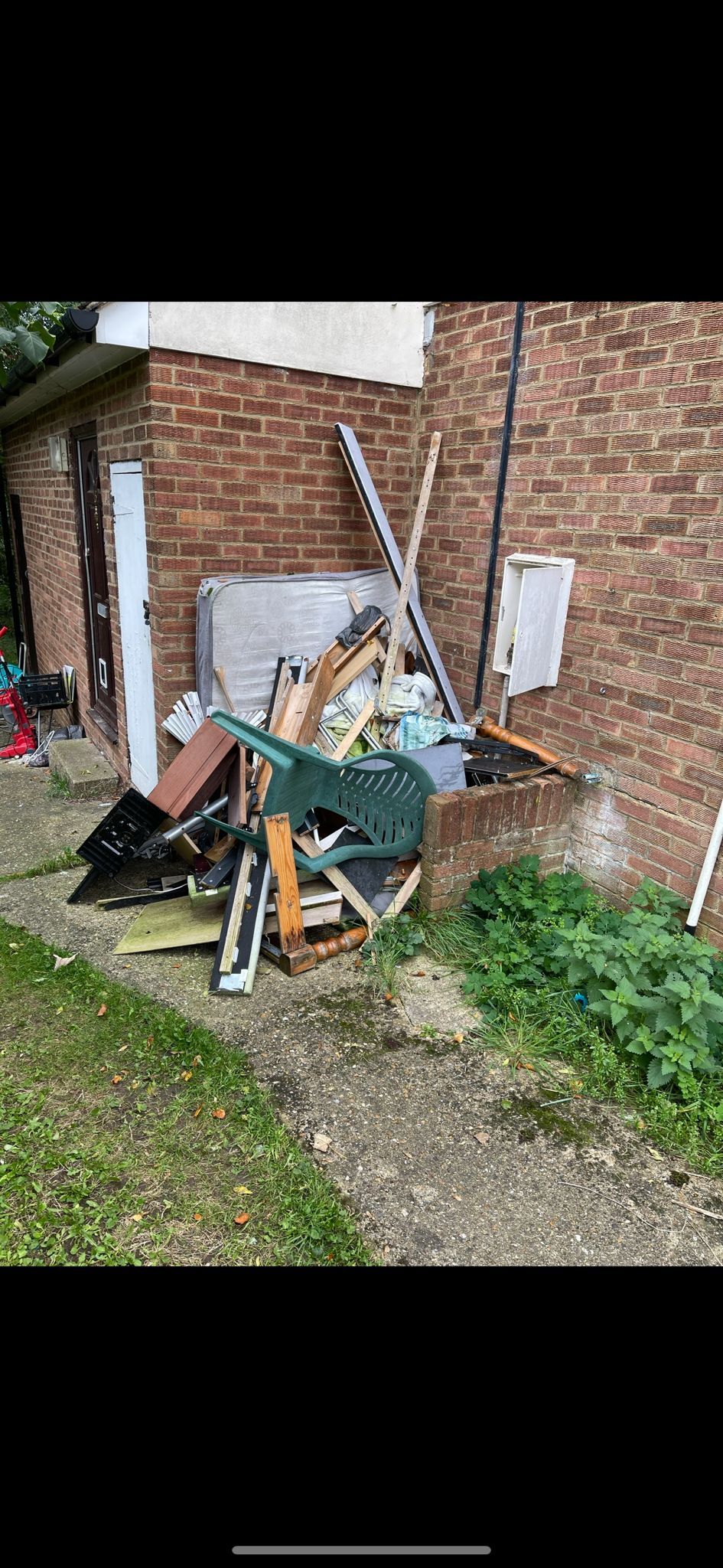 Pile of discarded items next to a brick wall and a small green plant.