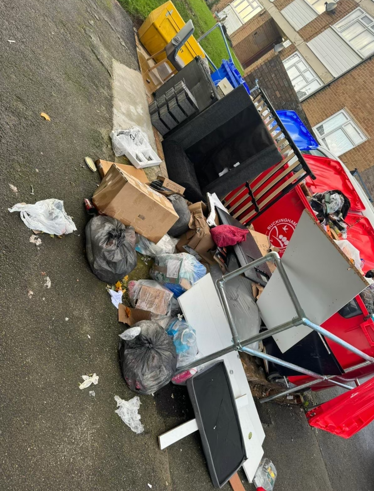 Pile of trash and discarded furniture on a paved area, including bags, boxes, and a desk.