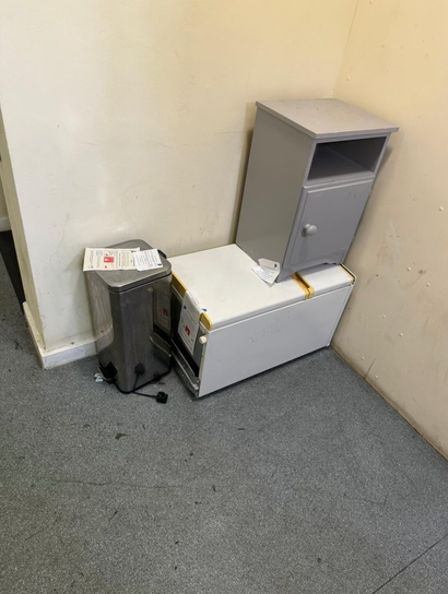 Gray cabinet and appliance on white rectangular base against a beige wall.