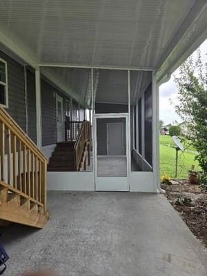 Covered porch with concrete floor, screened door, and wooden stairs beside a grassy yard.