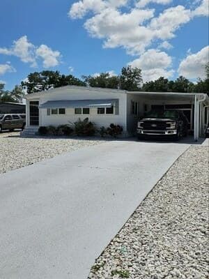 Modern single-story house with a white driveway, rock landscaping, and a car parked in the carport.