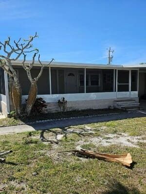 Damaged house exterior with broken tree branches and debris in the front yard