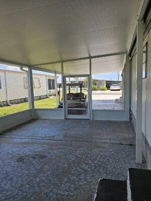Covered patio with textured concrete floor and glass doors, looking out to a driveway and neighboring houses.
