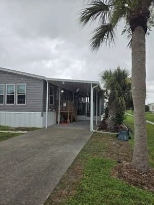 Mobile home with driveway, covered porch, and palm trees on a cloudy day