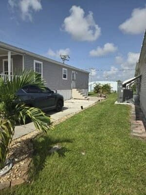 Narrow grassy side yard between two houses with a black car parked by the left house under a blue sky.
