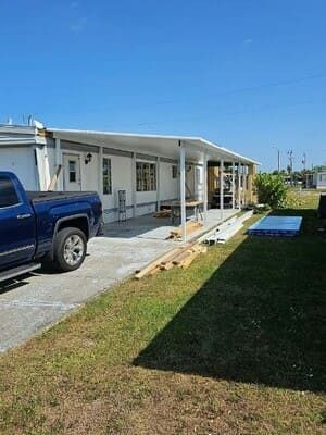 White house exterior with a covered porch, blue pickup truck, and a long ramp leading to the yard.