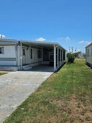White mobile home with covered porch beside a concrete driveway and grassy yard under a blue sky