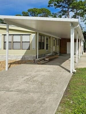 Covered ramp leading to a beige building entrance with white posts and a concrete driveway.