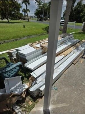 Stacked white metal beams and debris beside a sidewalk in a grassy park area