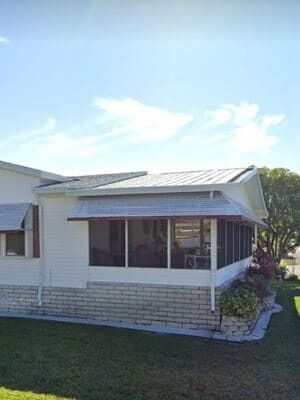 White house exterior with screened porch, brick foundation, and a grassy yard under a bright blue sky