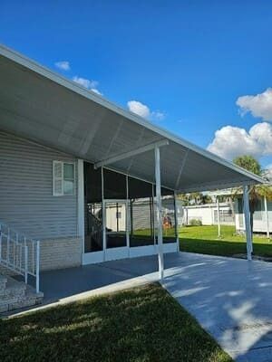 Covered walkway beside a brick building with white support posts, concrete path, and grassy lawn under a blue sky
