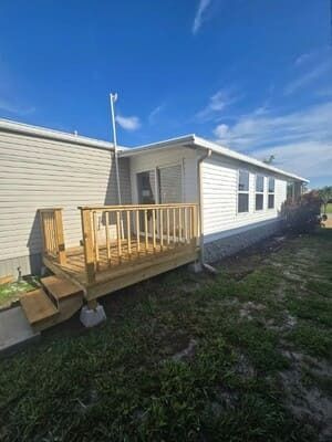 Small wooden deck with ramp attached to a beige mobile home under a blue sky.