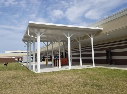Outdoor school entrance with white canopy and columns beside a brick building under a blue sky