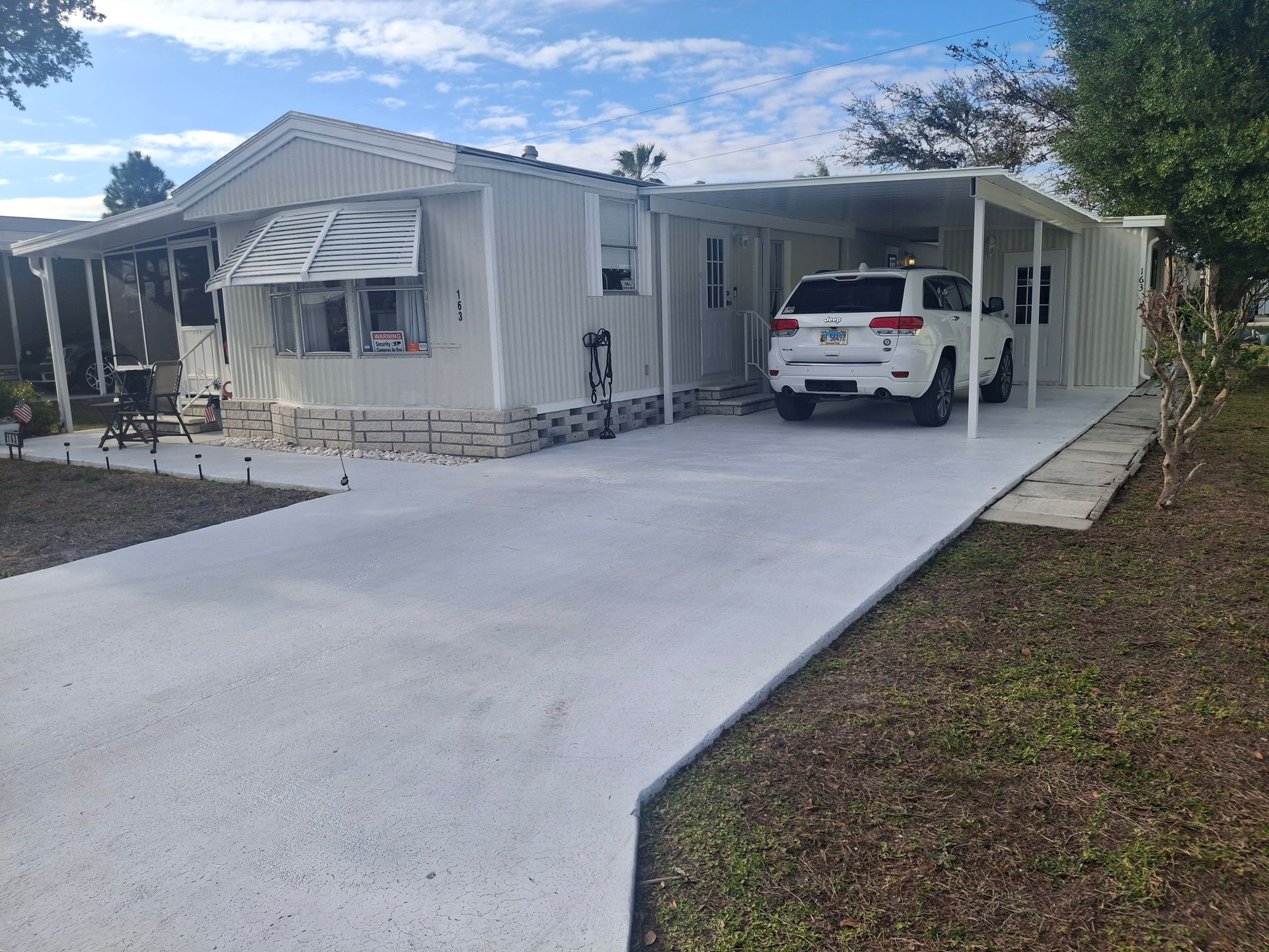 Single-story house with a long concrete driveway and a white SUV parked under a carport.