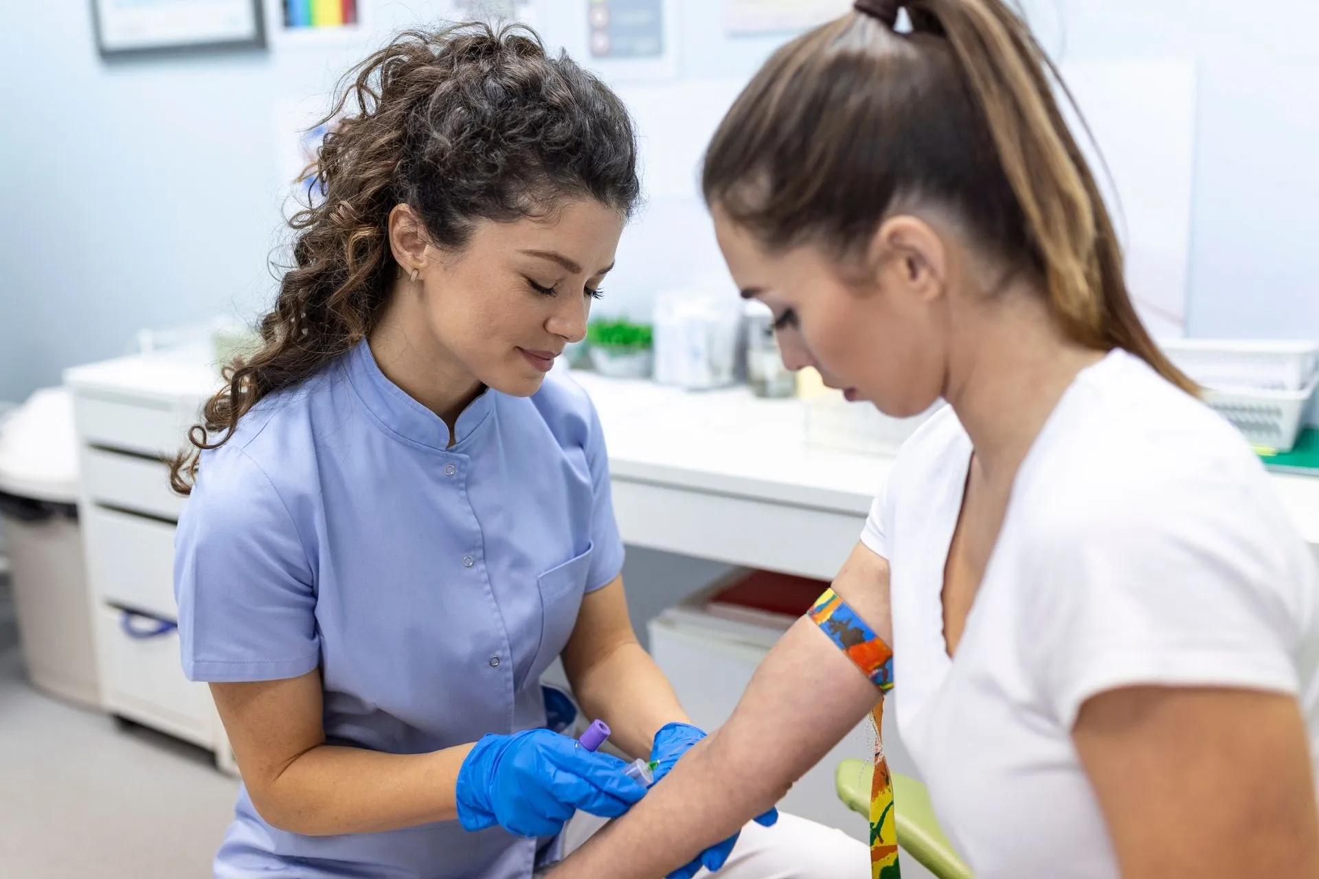 Phlebotomist drawing blood from a patient's arm. Medical setting, blue gloves and uniform.
