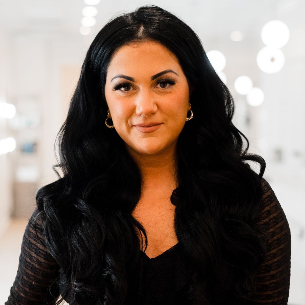 Woman with long dark hair in a softly lit indoor setting, looking at the camera with a slight smile