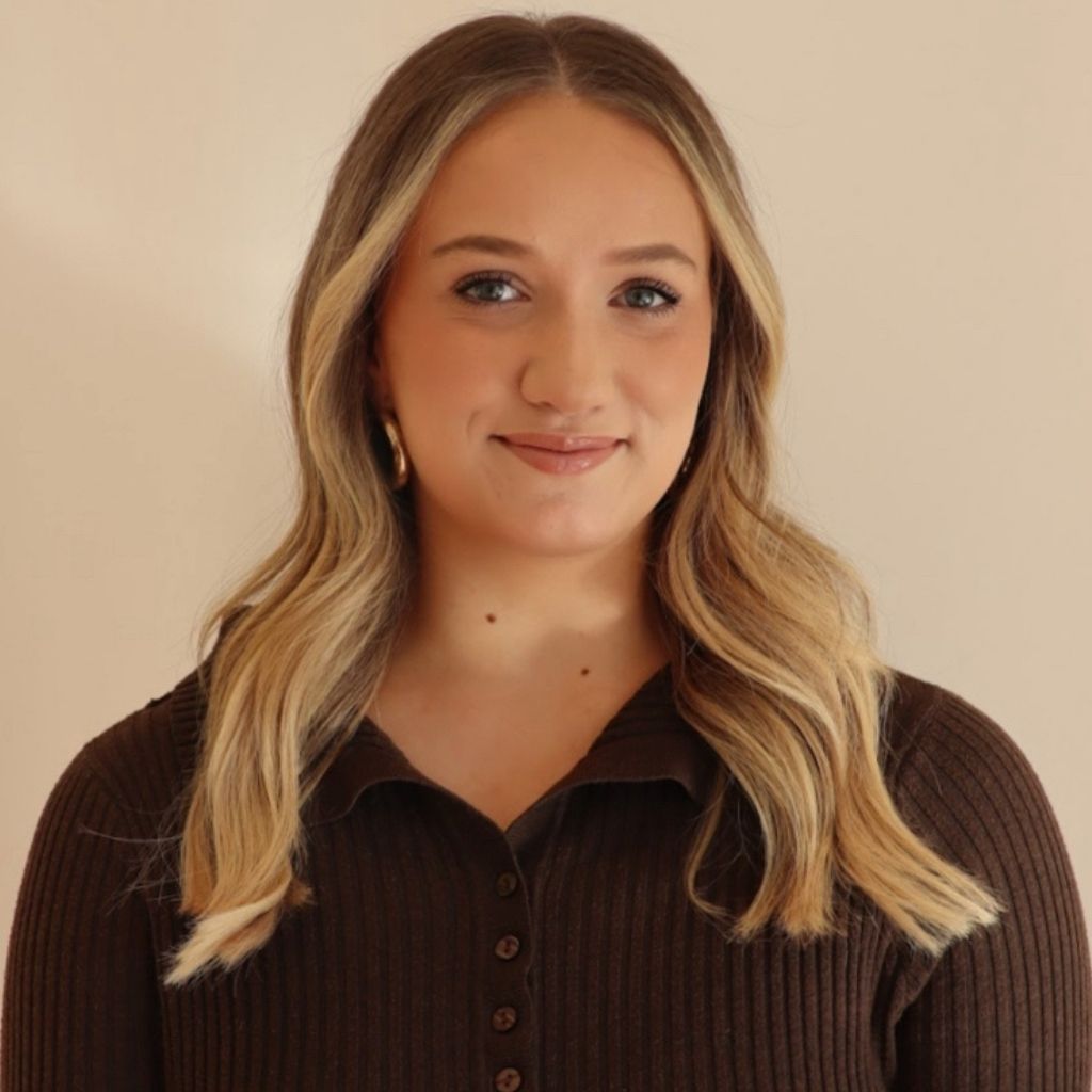 Portrait of a woman with blonde hair wearing a dark brown top against a beige background