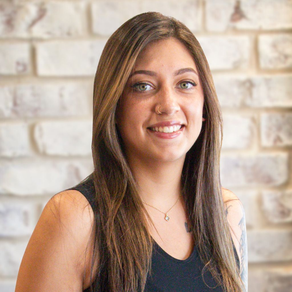 Young woman smiling in a dark top against a light brick wall