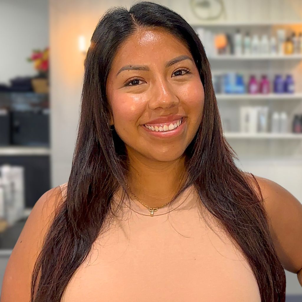 Smiling woman with long dark hair in a peach top, standing in a bright salon setting
