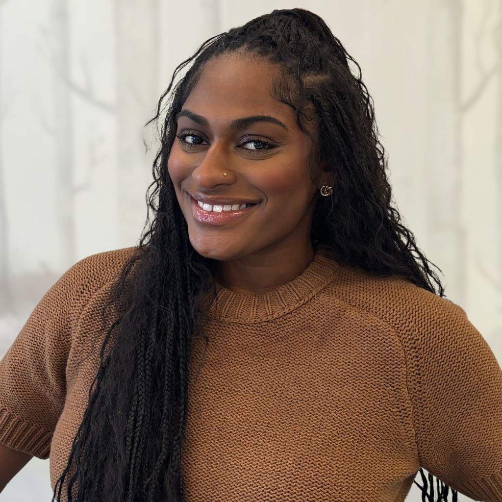 Smiling woman in a brown sweater against a light indoor background