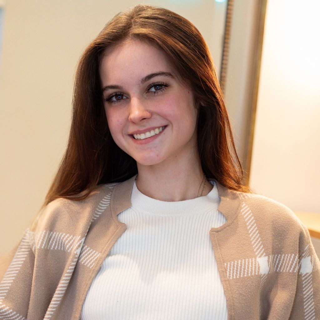 Smiling woman in a beige cardigan and white top indoors by a window
