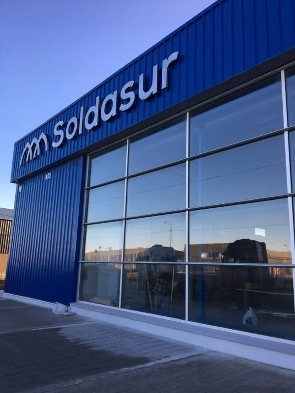 Fachada de Soldasur con fachada azul y grandes ventanales que reflejan la calle.