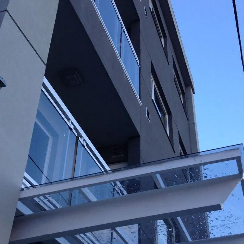 Edificio de apartamentos moderno con balcones de cristal contra un cielo azul.