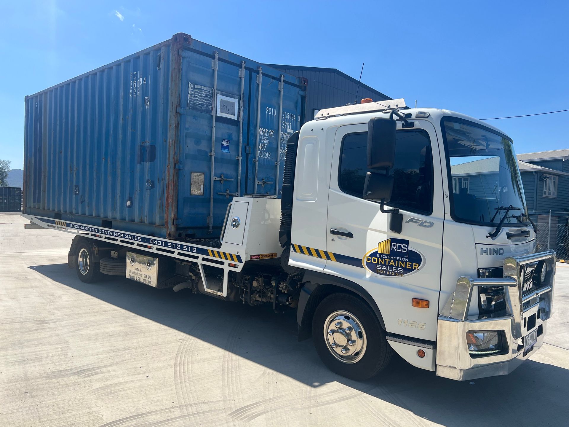 a Flatbed Truck Carrying a Blue Shipping Container on a Paved Surface — Rockhampton Container Sales in Kawana, QLD