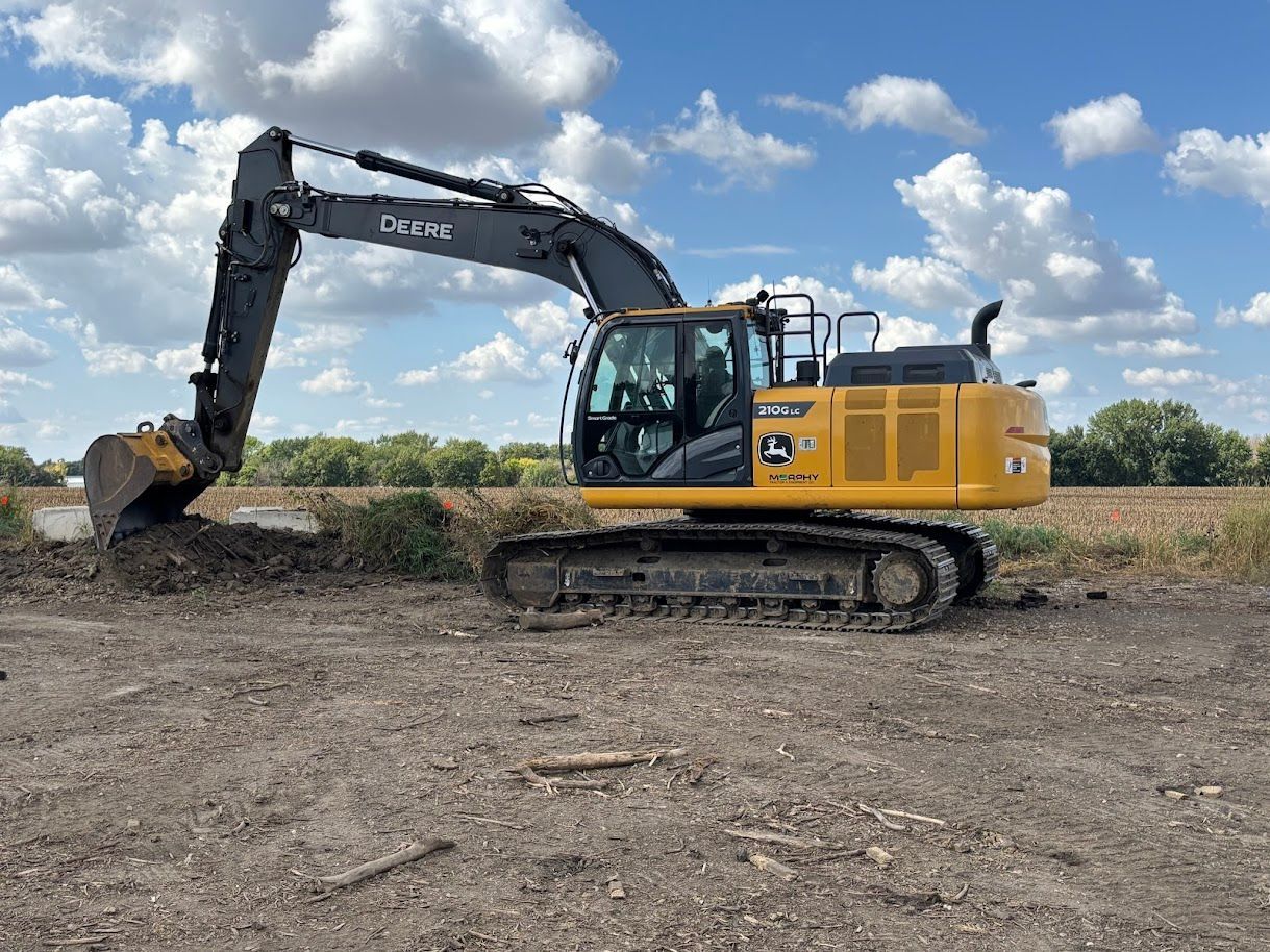 Yellow tracked excavator digging on a dirt field under a cloudy sky