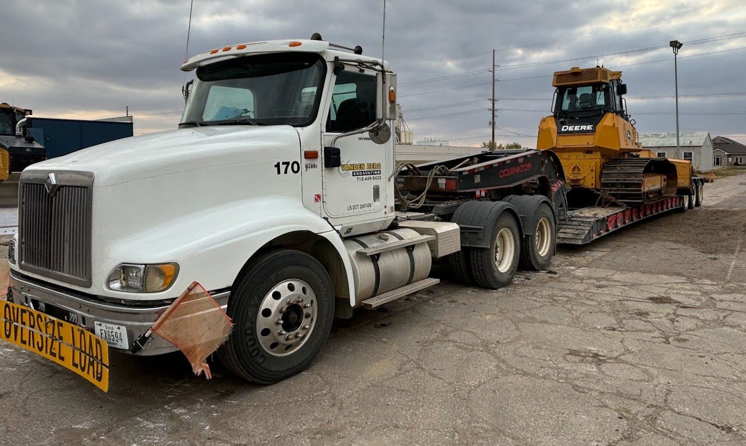 White semi truck hauling a yellow bulldozer on a flatbed trailer in a gravel lot