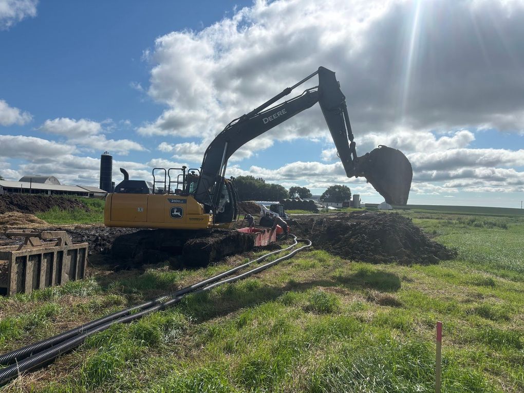 Yellow excavator digging a dirt mound in a grassy field under a cloudy sky