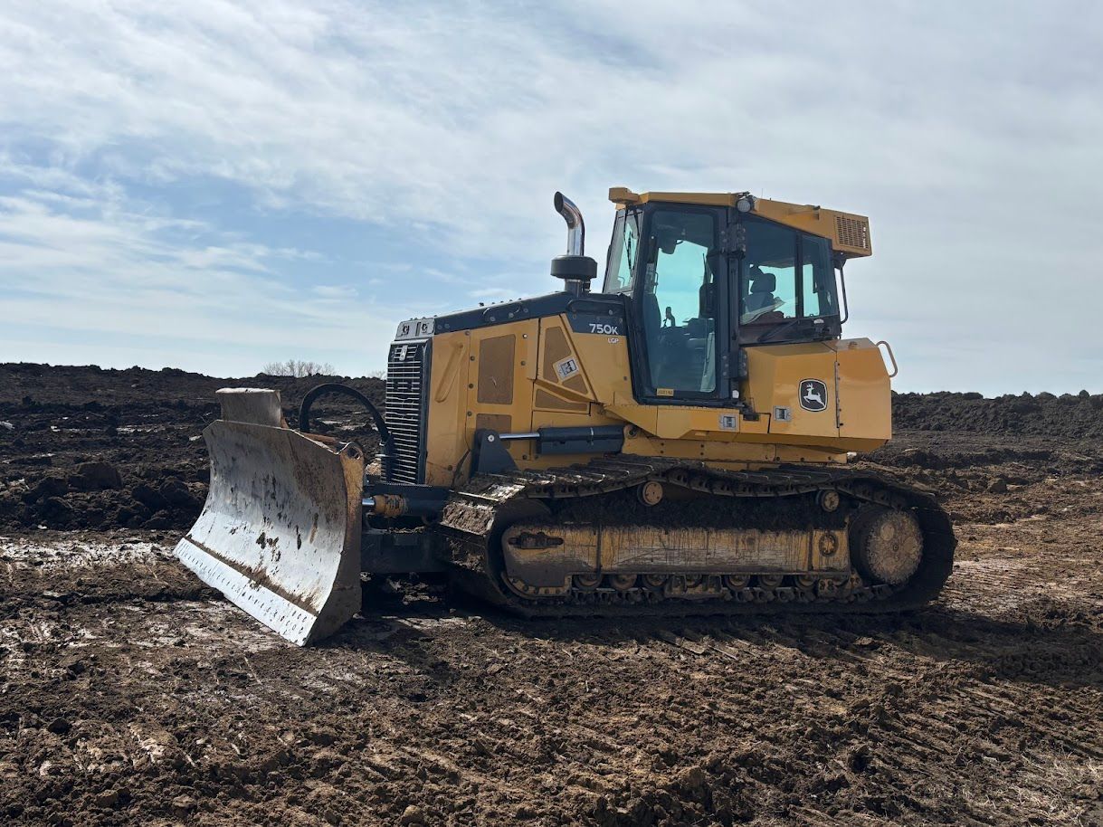 Yellow bulldozer with a front blade on muddy construction ground under a cloudy sky