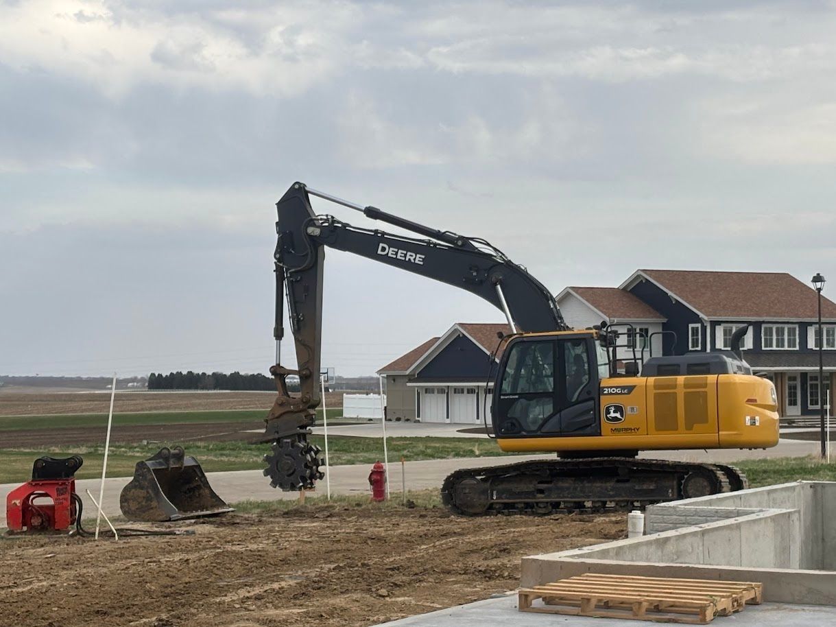 Yellow excavator working at a construction site near houses under a cloudy sky