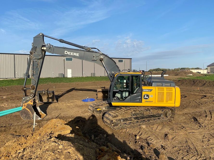 Yellow excavator digging in a muddy construction site beside a building under a blue sky